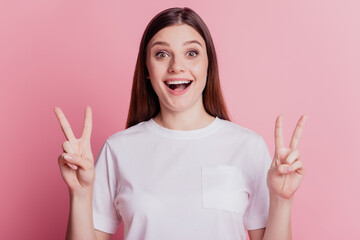 Lovely friendly excited girl show two peace gesture on pink background