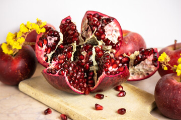 ruby red, juicy pomegranate open on a table with apple and dry yellow flowers