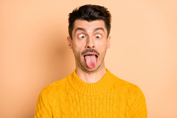 Photo portrait of grimacing silly man showing tongue fooling isolated on pastel beige color...