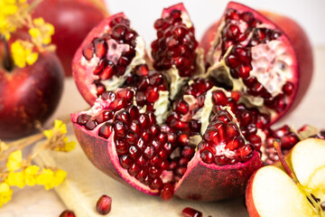 ruby red, juicy pomegranate open on a table with apple and dry yellow flowers