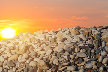 Fototapeta na wymiar heap of marine pebbles in light of red evening sun, sea coast natural background