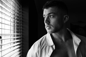 Portrait of handsome man with beard standing next to window with open shirt