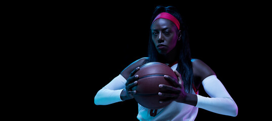 Beautiful african-american female basketball player in motion and action in neon light on black background. Concept of healthy lifestyle, professional sport, hobby.
