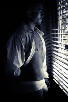 Portrait of handsome man with beard standing in front of window with open shirt and in underwear