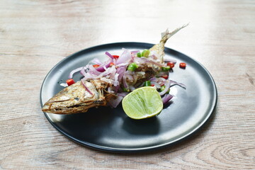 deep fried salty mackerel fish topping chop shallot and chili with slice lemon on plate