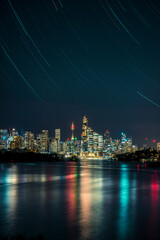 City skyline at night with water reflections and star trail