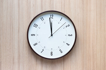 brown plastic clock on light wooden wall. show time in midday. concept : time for appointment or having lunch.
