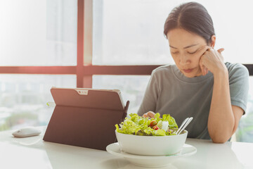 Selected focus on bowl of vegetable salad with woman working on laptop.