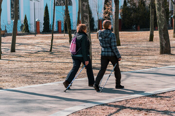 Two woman walks together in the park using tourists sticks. Back view. Strolling through the...