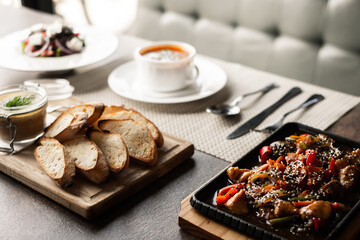 A hearty lunch in a cafe on the table, pate with croutons, bograch, Greek salad and a frying pan with veal. lunch for one person. dishes. kitchen.