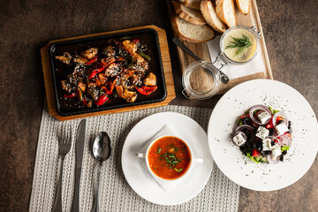 A hearty lunch in a cafe on the table, pate with croutons, bograch, Greek salad and a frying pan with veal. lunch for one person. dishes. kitchen.