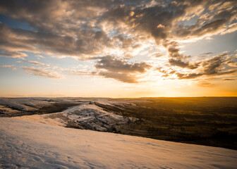 Fototapeta na wymiar Mam Tor Hill top Derbyshire Mountain range peaks covered deep winter snow at sunrise with beautiful orange golden light sky on freezing cold morning