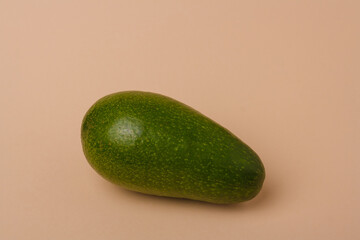 One whole green fresh avocado on beige background. Minimal styled composition.