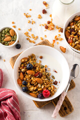 Homemade granola with nuts, berries, seeds and milk in white plate on table for healthy breakfast, top view