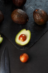 Ripe avocados in a basket on a black table, with a cut fruit and a stone.