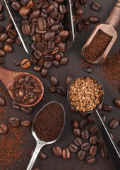 Various scoops with ground and bean coffee and freeze dried instant coffee granules on brown background.