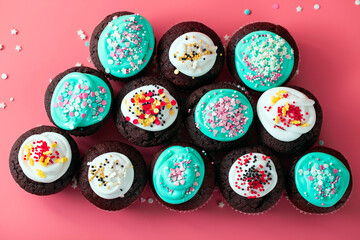 Lots of sugar muffins with icing and sugar sprinkles on a pink background. Chocolate cupcakes for a holiday party, top view