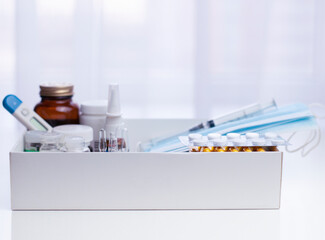 medicine background with glass ampoules, medicine bottle, pack of pills, medical masks, bandage, syringe, digital thermometer, nasal spray in the box