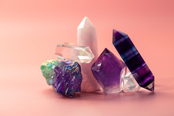 Various faceted crystals for healing and magical practices. A bunch of beautiful semi-precious stones. Amethyst, rose quartz, fluorite, rock crystal on a pastel pink background - obrazy, fototapety, plakaty