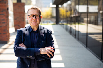 Handsome mature businessman standing on the street. Portrait of smiling manager. Successful business concept