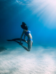Free diver with fins posing underwater over sandy bottom in blue ocean.