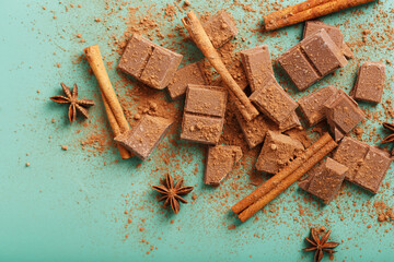 Chocolate broken into slices with cocoa powder and spices on a green background
