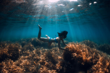 Woman free diver posing underwater in transparent sea with sun rays