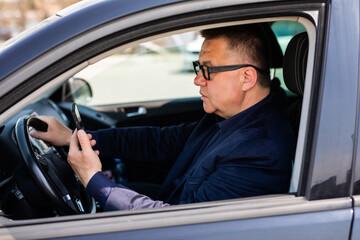 Middle-aged businessman sitting in his parked car and uses a mobile phone in a car.