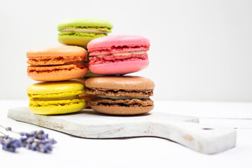 Colorful macaroons on a white wooden board and a bouquet of dried lavender.