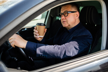 Fototapeta na wymiar Drinking on the go. Handsome middle age man sitting on the drivers seat of his car and drinking his morning coffee.