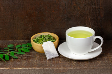 Obraz na płótnie Canvas Moringa Tea in white cup and fresh green leaf on brown wooden background. Moringa oleifera tropical herb healthy lifestyle concept.