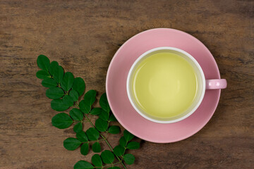Moringa Tea in white cup and fresh green leaf on brown wooden background, top view. Moringa oleifera tropical herb healthy lifestyle concept.