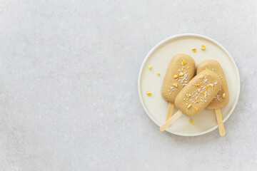 Popsicle with chocolate cashews, mango pieces and coconut on a plate. Sugar, gluten and lactose free. Horizontal orientation, copy space, top view.