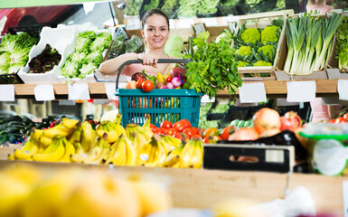 Young satisfied woman with basket filled with a fresh fruits and vegetables in the store