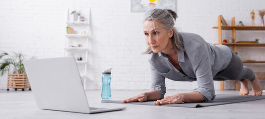 mature woman doing plank and looking at laptop, banner