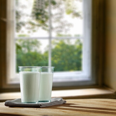 Two glasses full of milk. Wooden table with shadows and a napkin. home interior with a large window in the morning. Place for your product or inscription. 