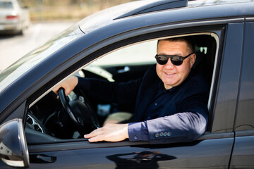 Fototapeta na wymiar Business trip. Confident senior businessman sitting in car and smiling at camera
