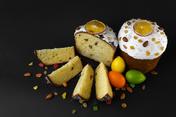 Traditional Easter cake on dark black background. Migdal, candied fruits, raisins, decor colorful eggs. Sectional view, slices, pieces. Orthodox treat. Top down view