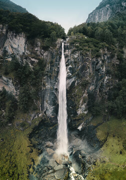 Aerial view of a majestic steep waterfall surrounded by lush forest in Cevio, Ticino, Switzerland.