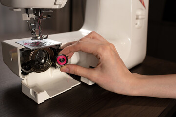 Sewing process on a sewing machine. Sewing accessories threads, graph paper, bobbin. Beautiful girl holding a bobbin.