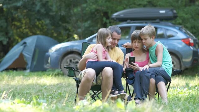 Young parents with their kids relaxing together at camping site browsing in smartphone.