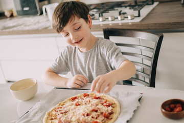 Little kid boy making pizza sitting at the table on the kitchen. Children helping in cooking lifestyle image