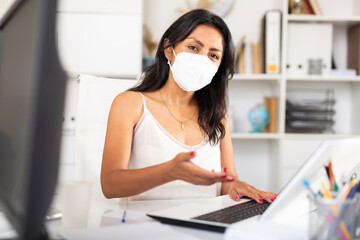 Latin business woman holding meeting in office in medical face mask to prevent spread of viral infection