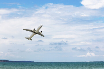 Fototapeta na wymiar Airplane flies over the sea and coast on white clouds background. Commercial plane taking off and gaining altitude, vacation and travel concept