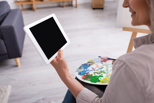 cropped view of happy mature woman holding palette and digital tablet with blank screen