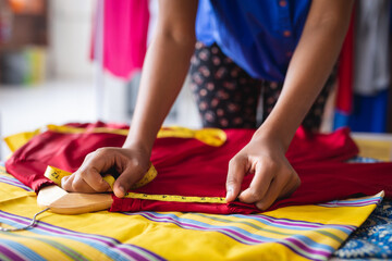 Mixed race fashion designer working in office measuring clothes on table