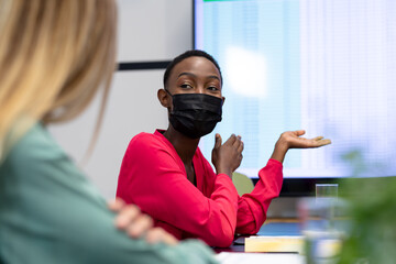 African american businesswoman wearing mask pointing at monitor