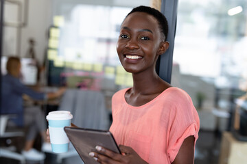 Portrait of happy african american businesswoman holding cup of coffee and digital tablet