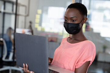 Obraz premium African american businesswoman wearing mask using laptop computer