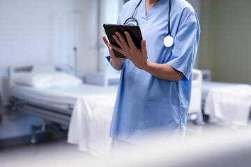 Midsection of caucasian female doctor in hospital wearing scrubs and stethoscope using tablet
